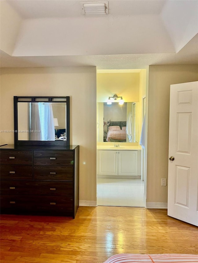 unfurnished bedroom with light tile patterned floors, a raised ceiling, and ensuite bath