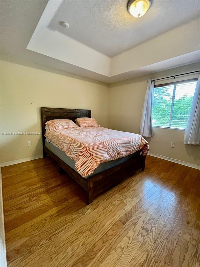 bedroom with wood-type flooring and a tray ceiling