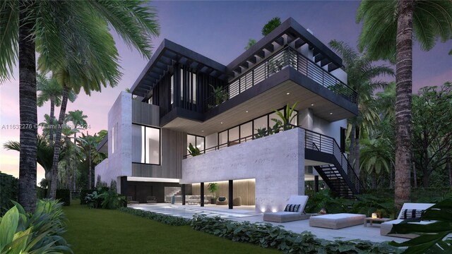 back house at dusk featuring a balcony, a patio, and a yard