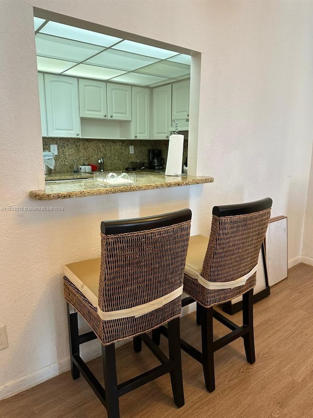 kitchen with green cabinetry, kitchen peninsula, light stone counters, and decorative backsplash