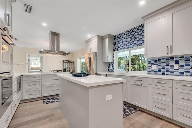 kitchen featuring tasteful backsplash, visible vents, a center island, ventilation hood, and light countertops