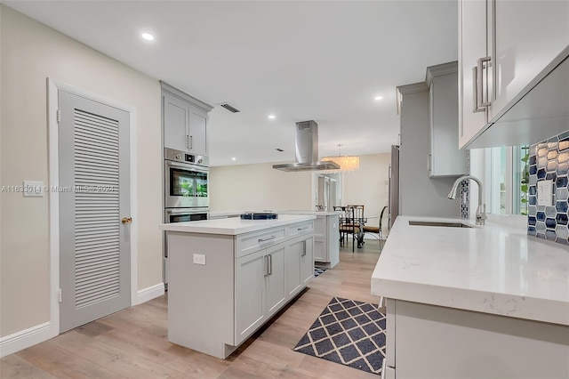 kitchen featuring visible vents, a kitchen island, stainless steel double oven, light wood-style flooring, and island exhaust hood