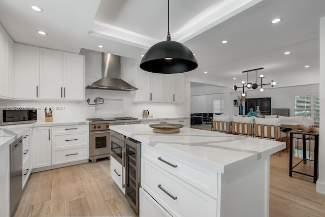 kitchen featuring white cabinetry, stainless steel appliances, hanging light fixtures, wine cooler, and wall chimney range hood