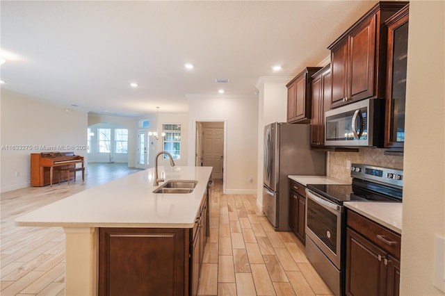 kitchen featuring light wood-type flooring, backsplash, stainless steel appliances, a kitchen island with sink, and sink