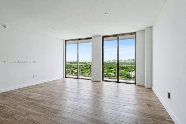 spare room with a wall of windows and light hardwood / wood-style flooring