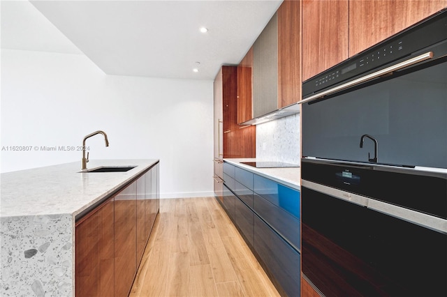 kitchen featuring black electric stovetop, light stone countertops, decorative backsplash, sink, and light hardwood / wood-style flooring