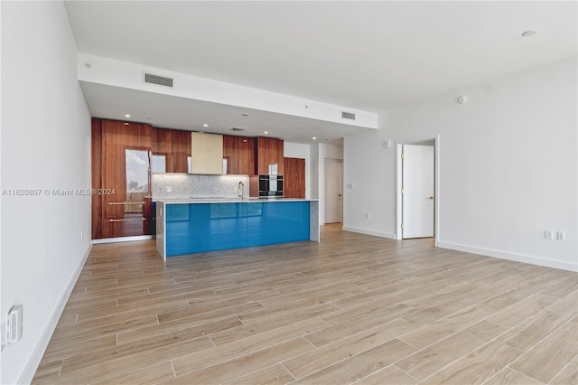 kitchen featuring light hardwood / wood-style floors, sink, tasteful backsplash, wall chimney exhaust hood, and oven