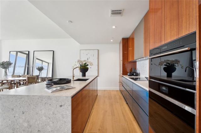 kitchen featuring black appliances, sink, a large island, and light hardwood / wood-style flooring