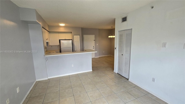 kitchen with kitchen peninsula, stainless steel fridge, light tile patterned floors, an inviting chandelier, and white cabinetry