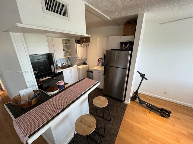 kitchen featuring white cabinetry, stainless steel fridge, light hardwood / wood-style floors, and a textured ceiling