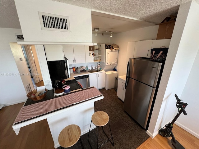 kitchen with stainless steel appliances, sink, rail lighting, a textured ceiling, and white cabinetry