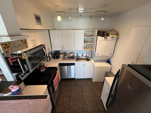 kitchen featuring white cabinets, stacked washer / drying machine, track lighting, appliances with stainless steel finishes, and sink