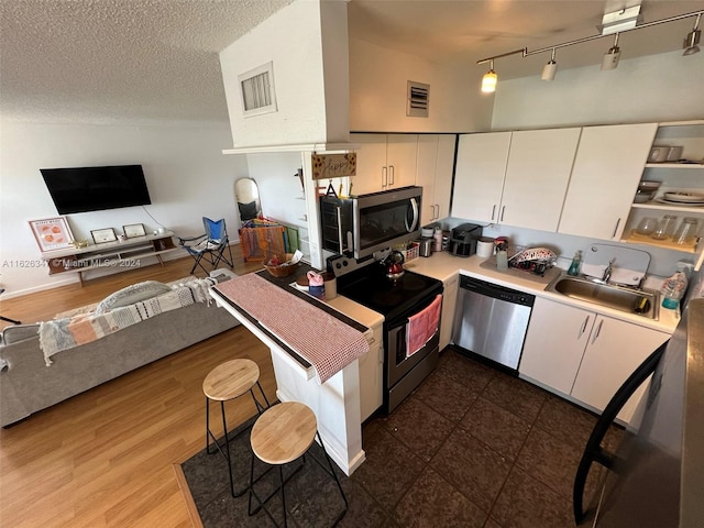 kitchen featuring appliances with stainless steel finishes, sink, rail lighting, white cabinetry, and dark wood-type flooring