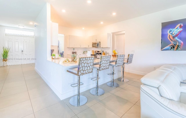 kitchen with light tile patterned flooring, white cabinetry, a kitchen bar, and kitchen peninsula