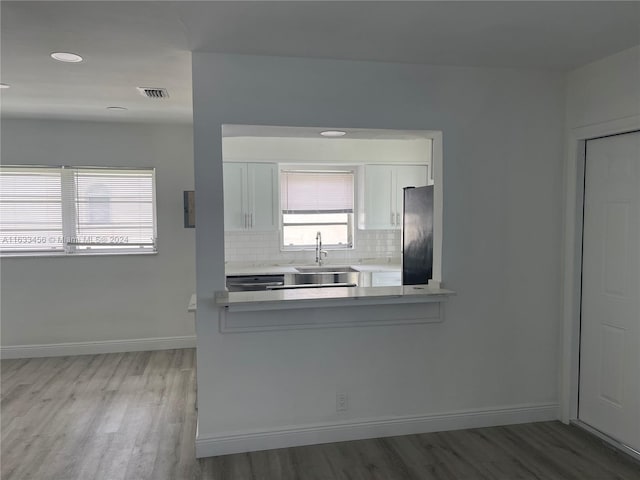 kitchen with white cabinetry, hardwood / wood-style flooring, sink, fridge, and backsplash