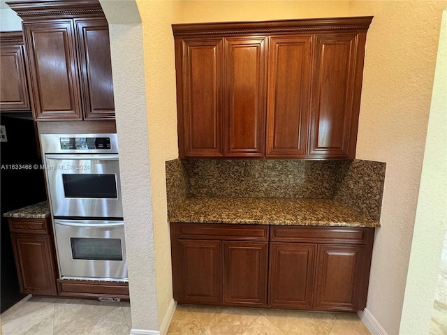 kitchen with dark stone countertops, stainless steel double oven, backsplash, and light tile patterned floors