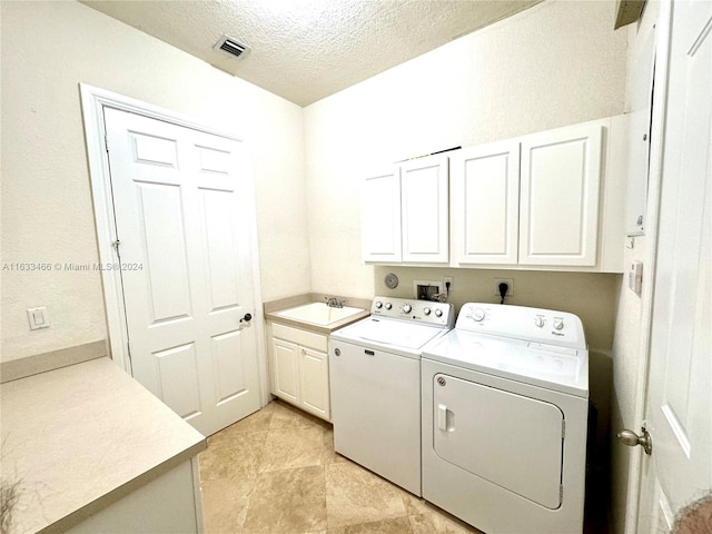 clothes washing area featuring cabinets, a textured ceiling, and separate washer and dryer