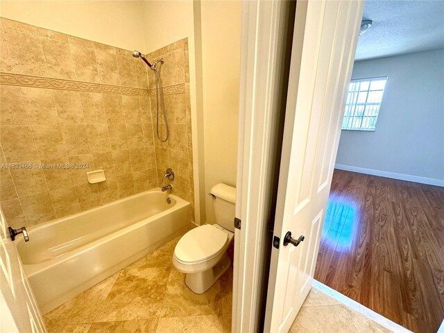 bathroom with wood-type flooring, a textured ceiling, tiled shower / bath, and toilet