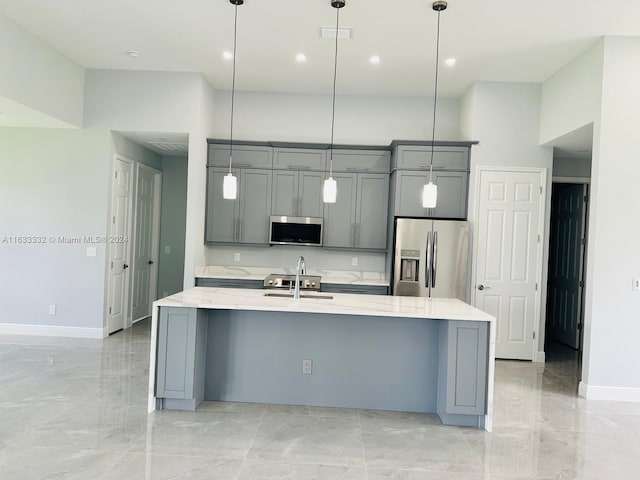 kitchen with an island with sink, hanging light fixtures, stainless steel appliances, and gray cabinets