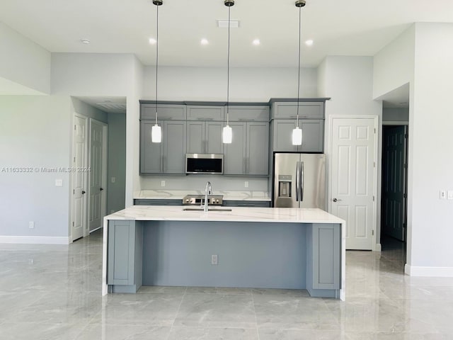 kitchen featuring gray cabinets, appliances with stainless steel finishes, decorative light fixtures, and a center island with sink