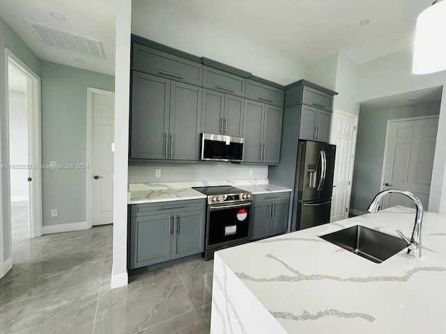 kitchen with gray cabinetry, light stone counters, stainless steel appliances, and sink