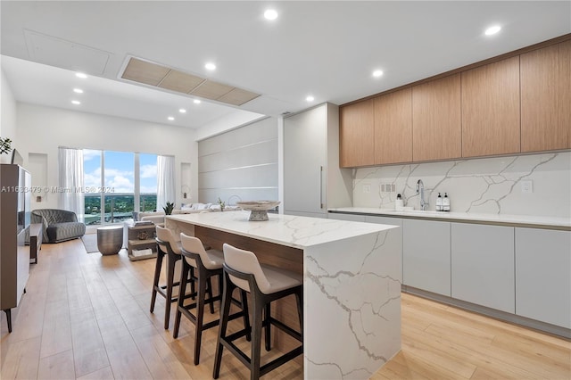 kitchen with light hardwood / wood-style flooring, tasteful backsplash, light stone counters, a kitchen island, and light brown cabinetry