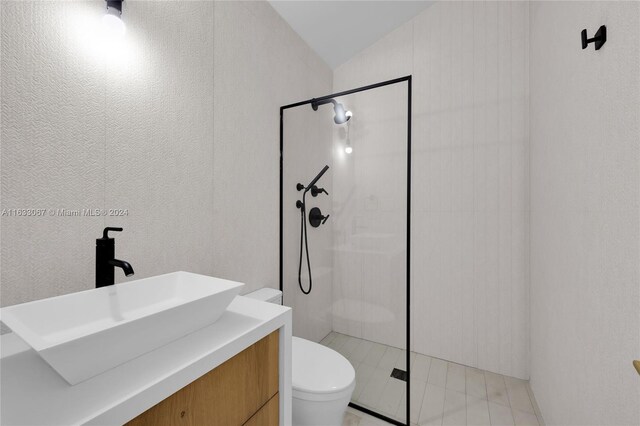 bathroom featuring lofted ceiling, vanity, toilet, and a tile shower