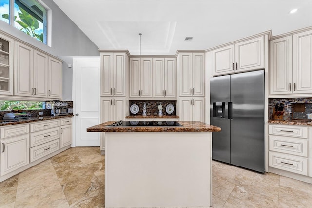 kitchen with stainless steel refrigerator with ice dispenser, black electric stovetop, a center island, dark stone counters, and backsplash