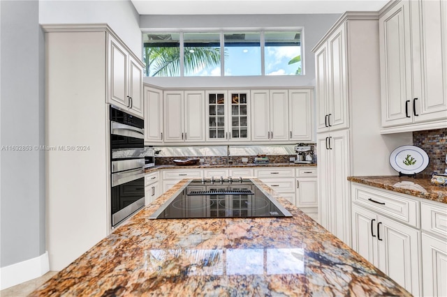 kitchen with double oven, a high ceiling, black electric stovetop, white cabinets, and dark stone counters