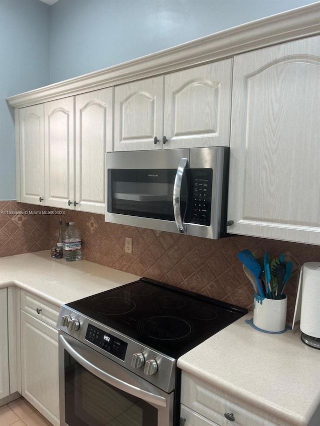 kitchen with appliances with stainless steel finishes, light tile patterned floors, cream cabinetry, and backsplash