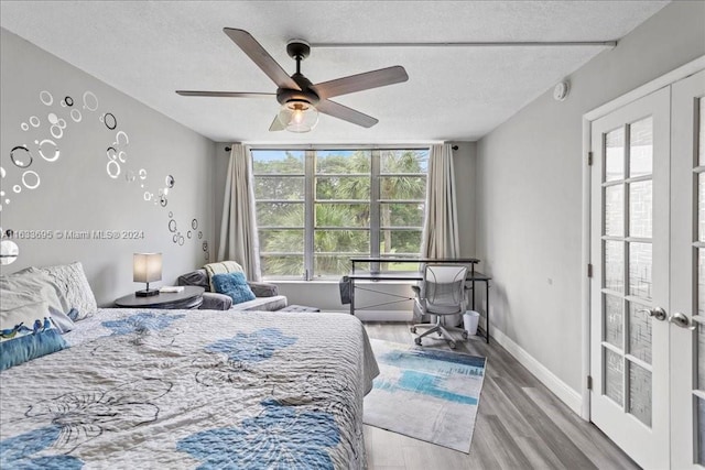 bedroom with a textured ceiling, wood-type flooring, ceiling fan, and french doors