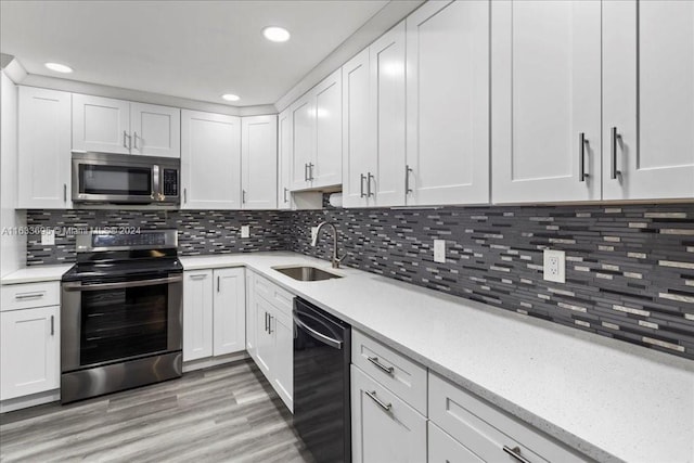 kitchen featuring appliances with stainless steel finishes, light hardwood / wood-style flooring, white cabinets, sink, and decorative backsplash