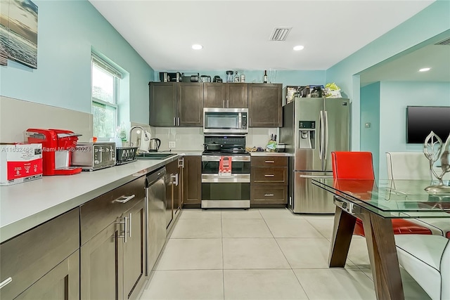 kitchen featuring appliances with stainless steel finishes, tasteful backsplash, sink, dark brown cabinets, and light tile patterned flooring