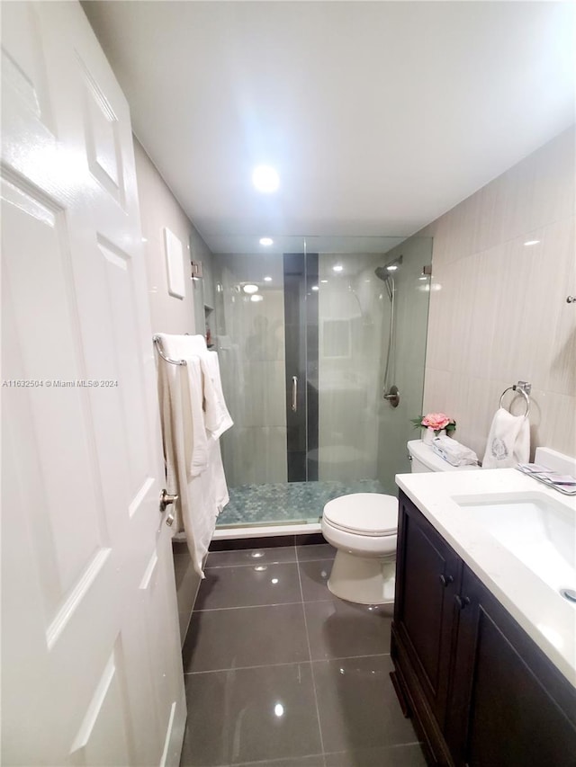 bathroom with vanity, walk in shower, tile walls, toilet, and tile patterned flooring