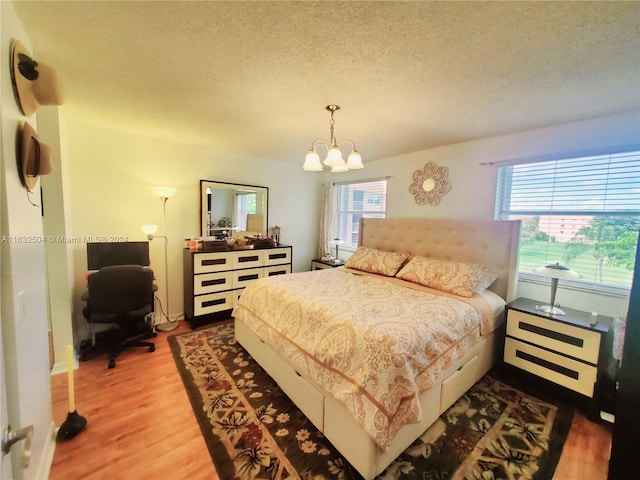 bedroom with multiple windows, a chandelier, hardwood / wood-style flooring, and a textured ceiling