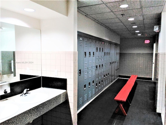 interior space with a drop ceiling, tile patterned flooring, tile walls, and dual bowl vanity