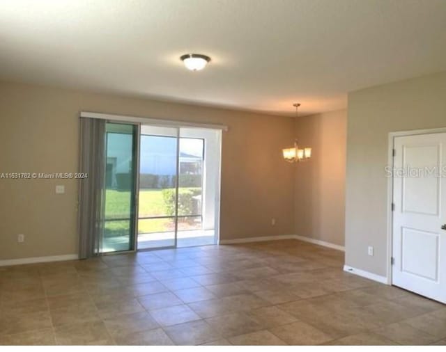 tiled spare room featuring an inviting chandelier