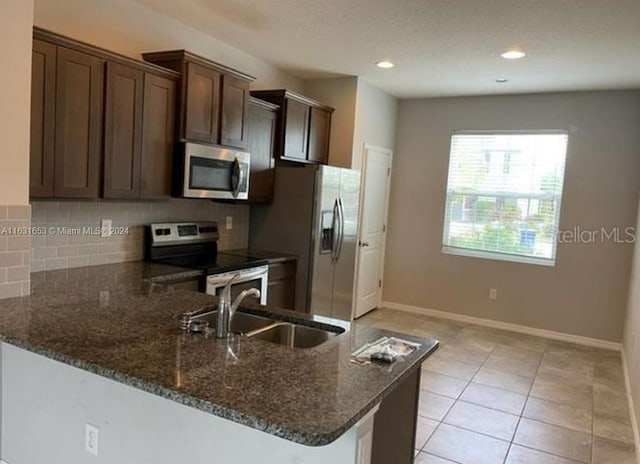 kitchen with stainless steel appliances, sink, dark brown cabinets, backsplash, and dark stone countertops