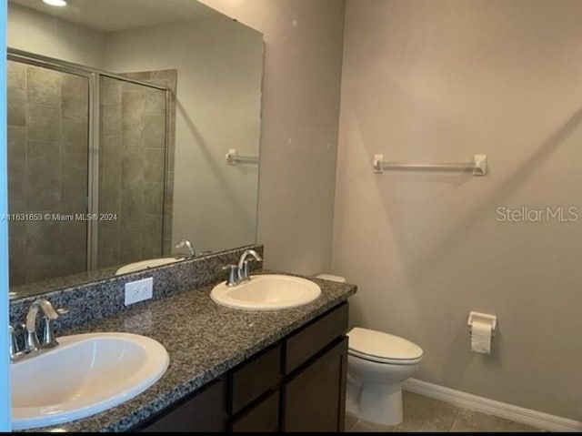 bathroom featuring a shower with shower door, toilet, tile patterned floors, and dual bowl vanity