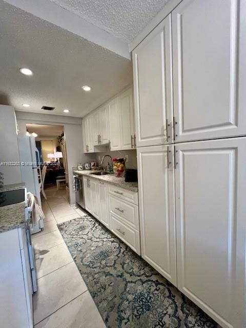 kitchen with light tile patterned floors, a textured ceiling, white cabinets, stainless steel dishwasher, and sink