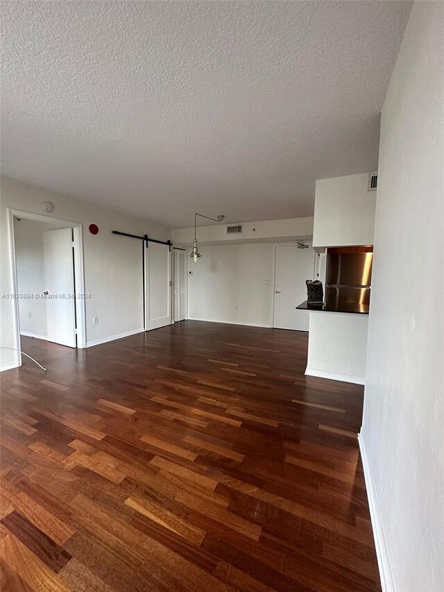 spare room featuring a barn door, a textured ceiling, and dark wood-type flooring