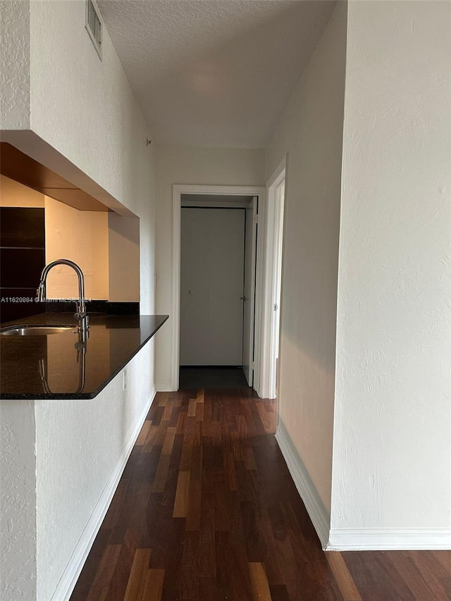 hall featuring sink, dark wood-type flooring, and a textured ceiling