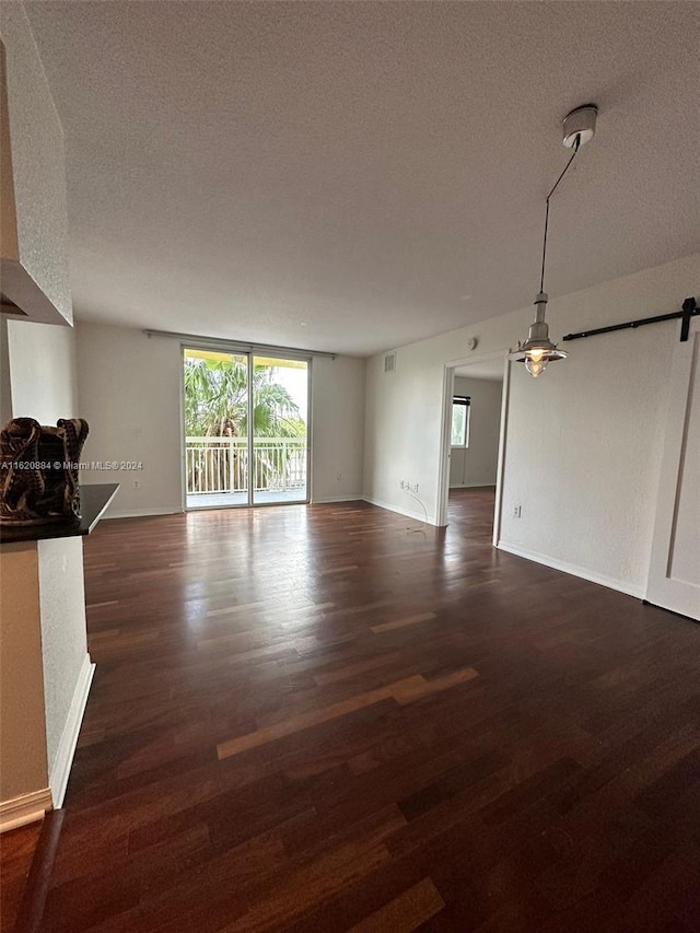 unfurnished living room with dark hardwood / wood-style flooring, a barn door, and a textured ceiling