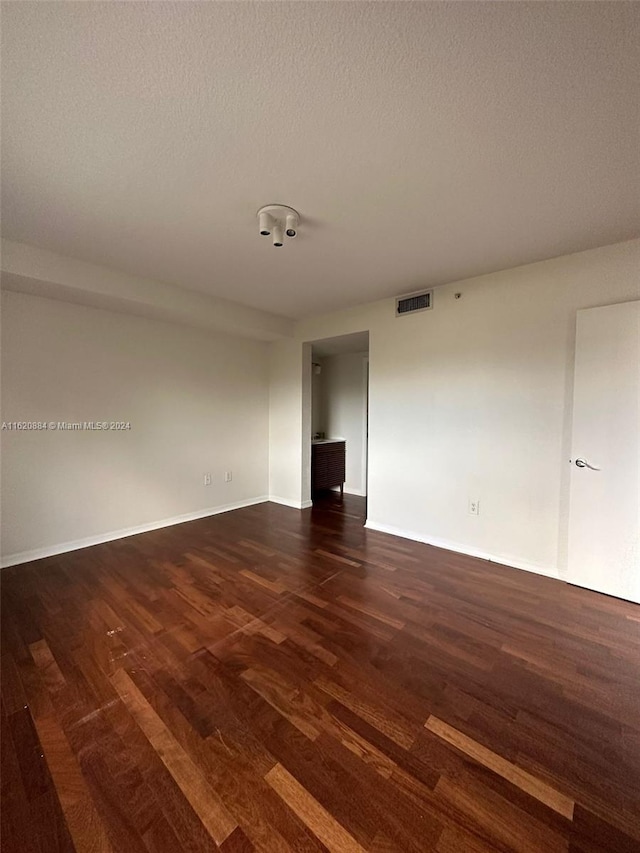 unfurnished room featuring dark wood-type flooring and a textured ceiling