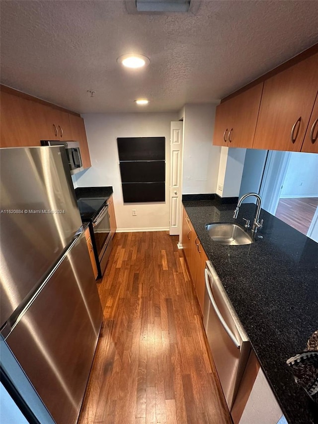 kitchen with appliances with stainless steel finishes, a textured ceiling, dark stone counters, dark hardwood / wood-style flooring, and sink