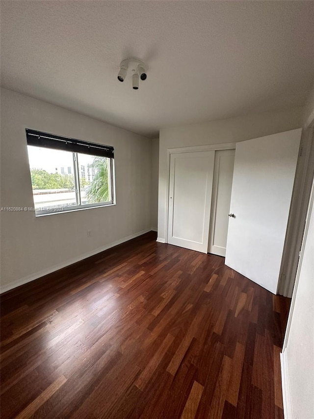 unfurnished bedroom featuring dark hardwood / wood-style flooring, a textured ceiling, and a closet