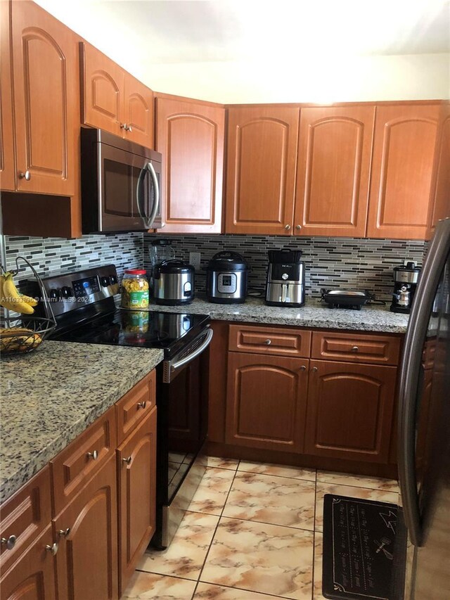 16700 NW 55th Ave Unit 12, Miami Gardens, FL 33055 - kitchen featuring appliances with stainless steel finishes, brown cabinetry, light stone counters, and tasteful backsplash
