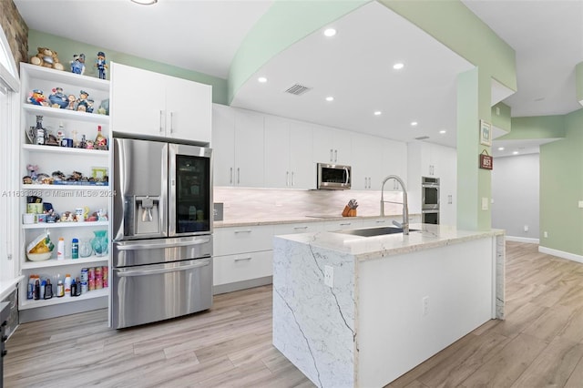 kitchen with appliances with stainless steel finishes, an island with sink, sink, white cabinets, and light stone counters