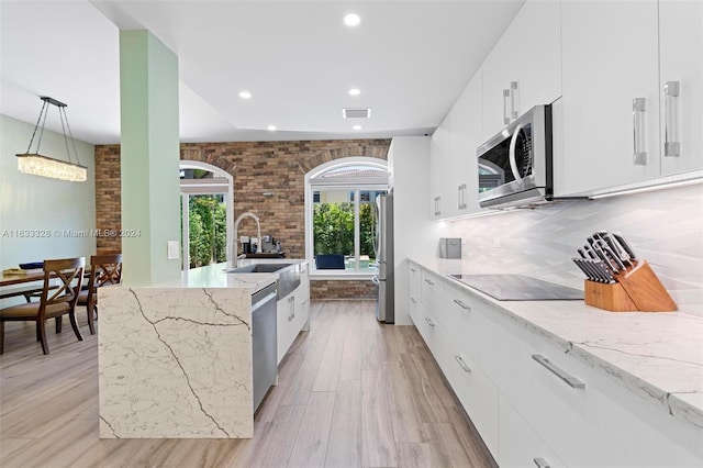 kitchen featuring sink, appliances with stainless steel finishes, backsplash, light stone counters, and decorative light fixtures