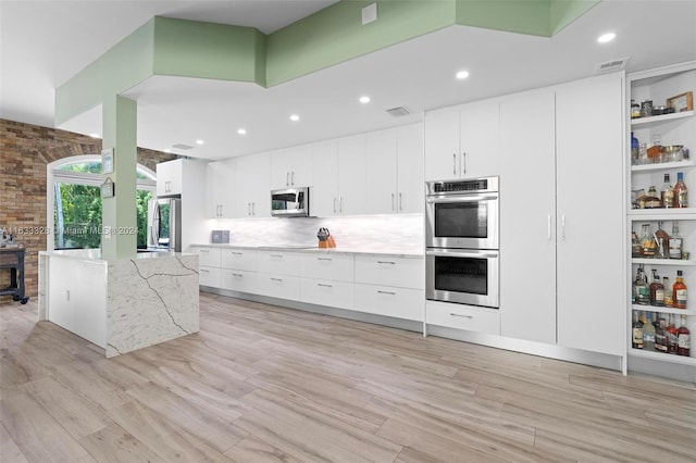 kitchen with backsplash, white cabinets, light stone counters, stainless steel appliances, and light hardwood / wood-style flooring